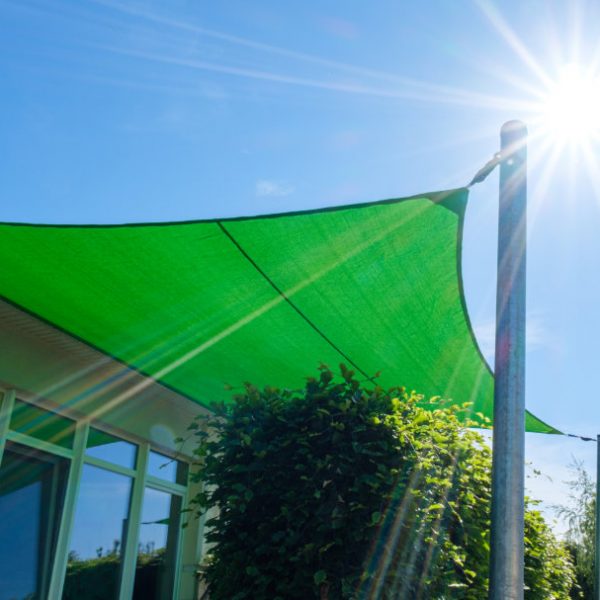 Wie befestigt man ein Sonnensegel? Grünes Segel mit Keder am Haus und an zwei Pfosten befestigt